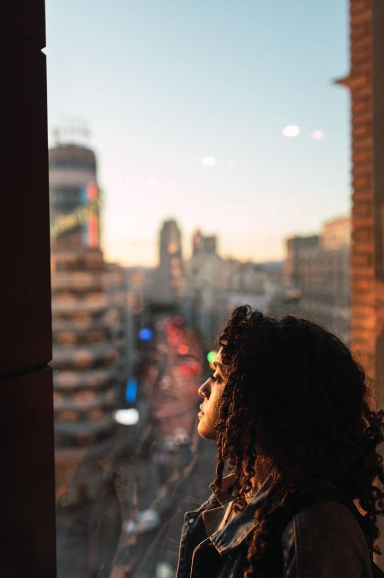 Mujer de perfil viendo por la ventana un paisaje urbano