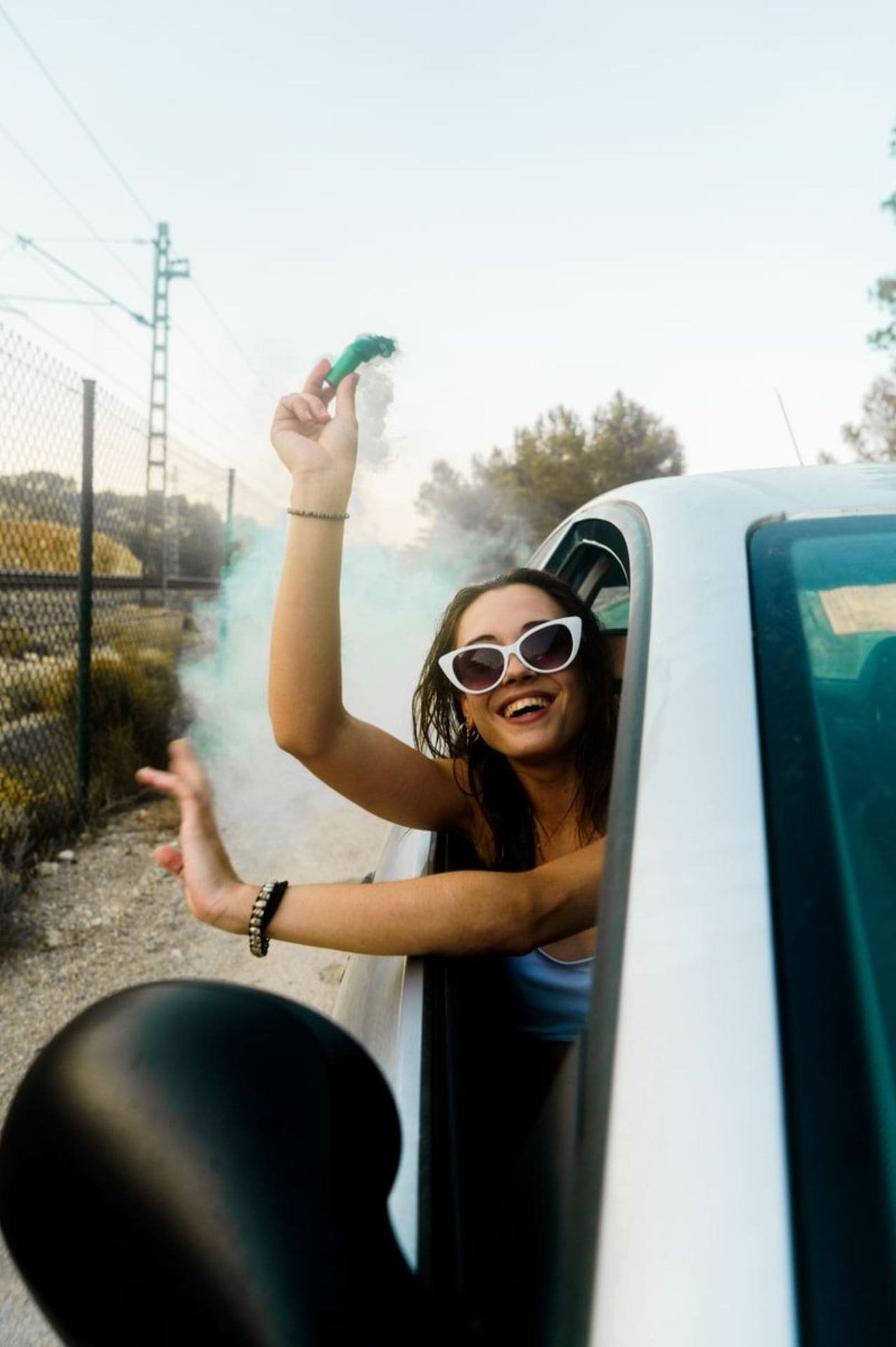 Mujer asomándose por la ventanilla de un auto y con una bengala en la mano